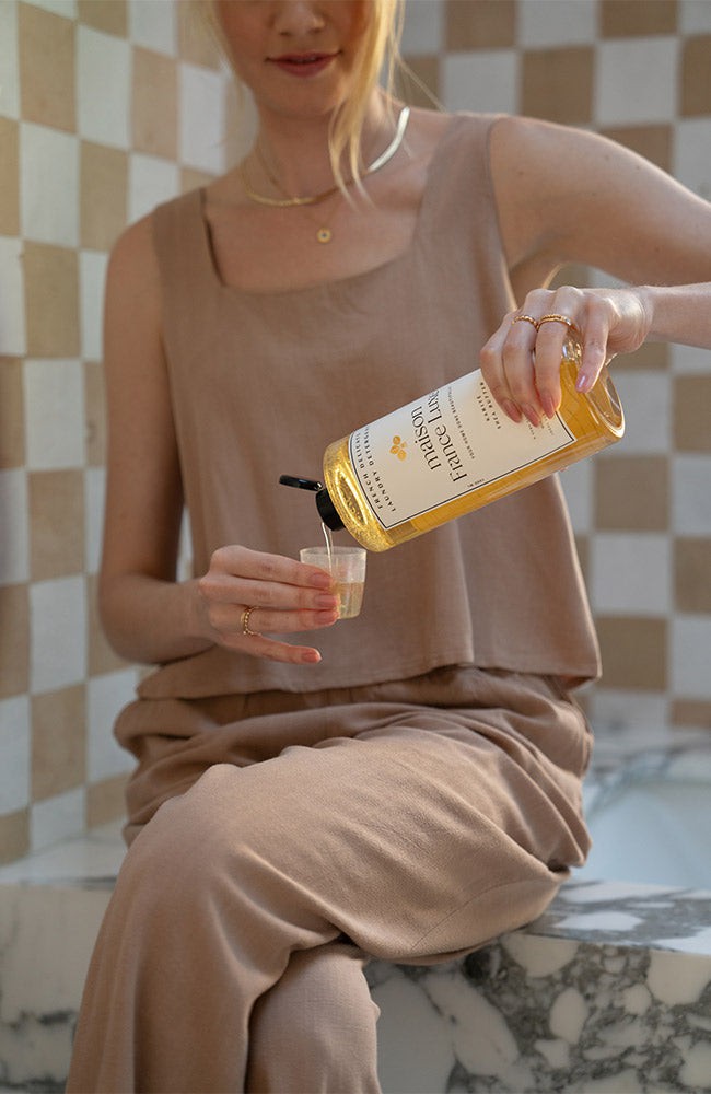 Person pouring laundry detergent from a bottle into a cup against a checkered wall.