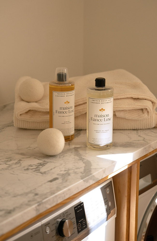 Two bottles of Maison Française laundry products on a marble countertop with towels in the background.