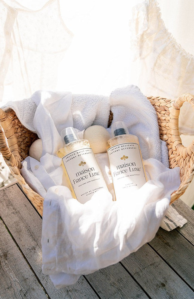 Two bottles of 'maison francis leclerc' products in a basket with white towels on a wooden surface.
