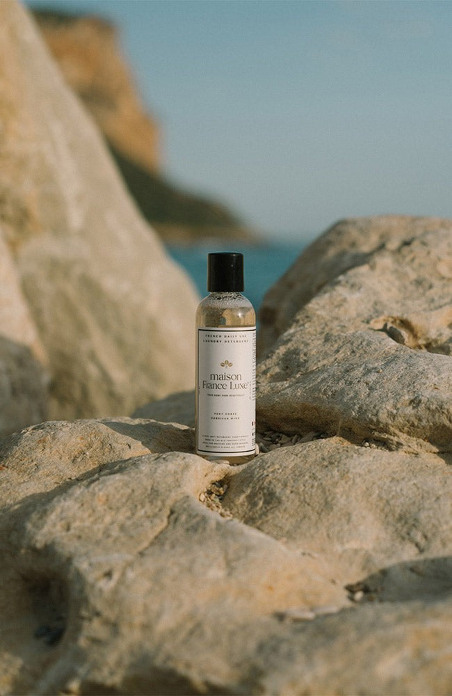 Bottle of 'The Maison' product on a rocky surface with a scenic background